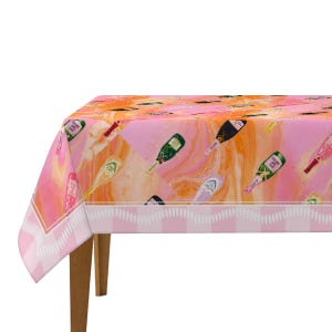 May include: A pink and orange tablecloth featuring a pattern of champagne bottles. The tablecloth has a white and pink striped border and is draped over a wooden table. The bottles are in various colors, including green, gold, and black.