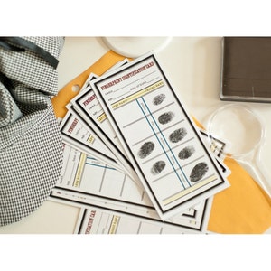 May include: A set of five fingerprint identification cards with a black and white design. The cards have spaces for name, age, date of birth, and fingerprints. The cards are on a yellow surface.