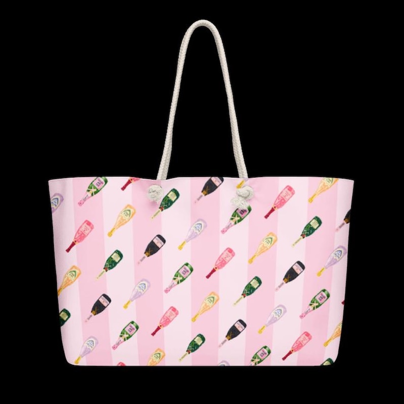May include: A large tote bag with a pink and white striped pattern. The bag is covered in a repeating pattern of champagne bottles in various colors. It has white rope handles.