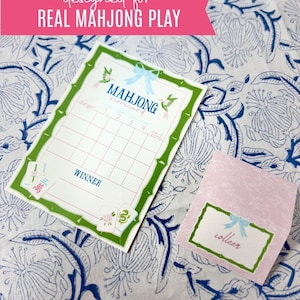 May include: A Mahjong scorecard and a pink name tag with the name "colleen" are displayed on a floral patterned surface. The scorecard has a green bamboo-style border and the text "designed for REAL MAHJONG PLAY".