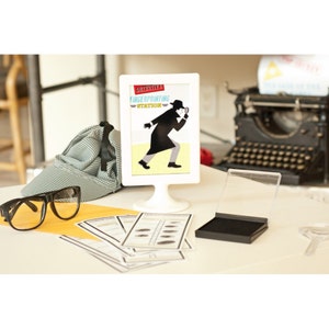 May include: A white framed sign with the text "Detective's Fingerprinting Station" and a silhouette of a detective with a magnifying glass. There is a black ink pad, a magnifying glass, and fingerprint cards on a white table.