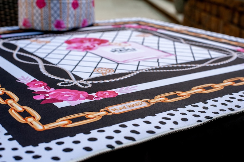 May include: A decorative mat with a black and white design, featuring gold chain links, pink roses, and a perfume bottle illustration. The mat has the words "PLAY RIGHT" on a gold plate.