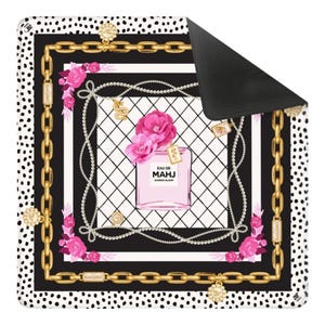 May include: A decorative mat featuring a perfume bottle design. The mat has a black and white polka dot border, a gold chain design, and a central image of a pink perfume bottle with the text "EAU DE MAHJ BAMBOO BLOOM".