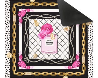 May include: A decorative mat featuring a perfume bottle design. The mat has a black and white polka dot border, a gold chain design, and a central image of a pink perfume bottle with the text "EAU DE MAHJ BAMBOO BLOOM".