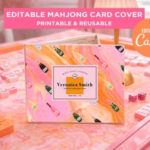 May include: A pink and orange mahjong card cover with a champagne bottle pattern. The cover has the text "EDITABLE MAHJONG CARD COVER PRINTABLE & REUSABLE" and "EDITABLE IN Canva". The center label reads "BIRD BAM CHEERS" and "Veronica Smith".