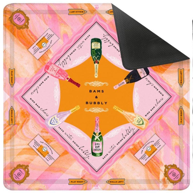 May include: A square, pink and orange mousepad with a champagne theme. The design features champagne bottles, labels, and the words "Bams & Bubbly". The mousepad has a black, non-slip backing.