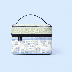 K&ouml;nnte beinhalten: Eine rechteckige Kosmetiktasche mit schwarzem Griff und Rei&szlig;verschluss. Die Tasche hat ein Blumenmuster mit blauen Hortensien und dem Text "PRETTY little TILES". Der obere Teil hat ein gr&uuml;nes Bl&auml;ttermuster.