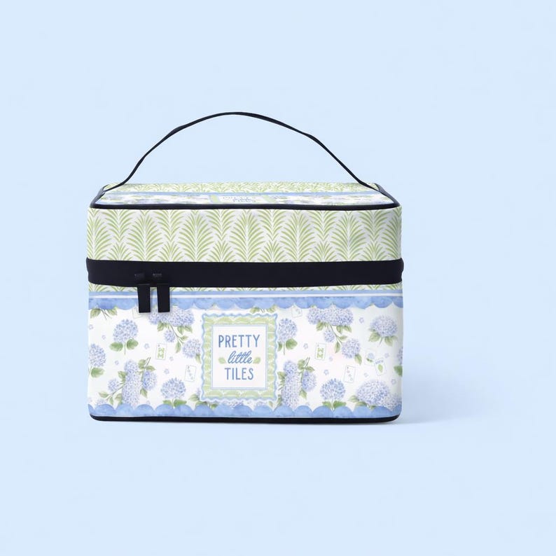 K&ouml;nnte beinhalten: Eine rechteckige Kosmetiktasche mit schwarzem Griff und Rei&szlig;verschluss. Die Tasche hat ein Blumenmuster mit blauen Hortensien und dem Text "PRETTY little TILES". Der obere Teil hat ein gr&uuml;nes Bl&auml;ttermuster.