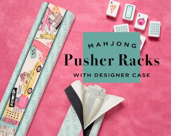 May include: Mahjong pusher racks with a designer case, featuring a New York City theme. The racks are light blue with a colorful design, and the case is open, revealing the clear plastic pusher. Mahjong tiles are also visible.