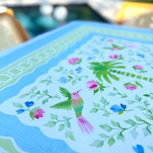 May include: A light blue tray with a scalloped edge and a floral design. The tray features a hummingbird, palm trees, and flowers in pink, blue, and green. The tray is likely made of a durable material.