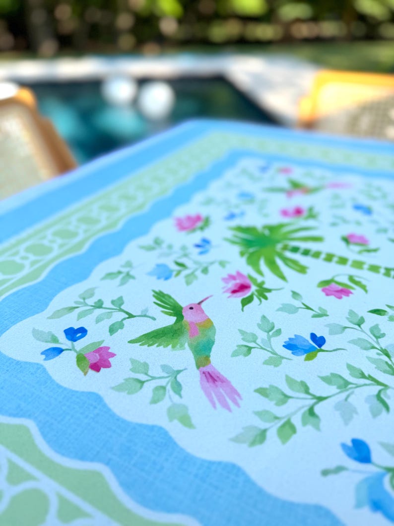 May include: A light blue tray with a scalloped edge and a floral design. The tray features a hummingbird, palm trees, and flowers in pink, blue, and green. The tray is likely made of a durable material.