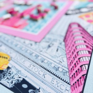 May include: A close-up of a light blue textile with a pink and white design. The design includes a pink building, the words "NEW YORK STOCK EXCHANGE", and a pink framed image with pink flamingos.