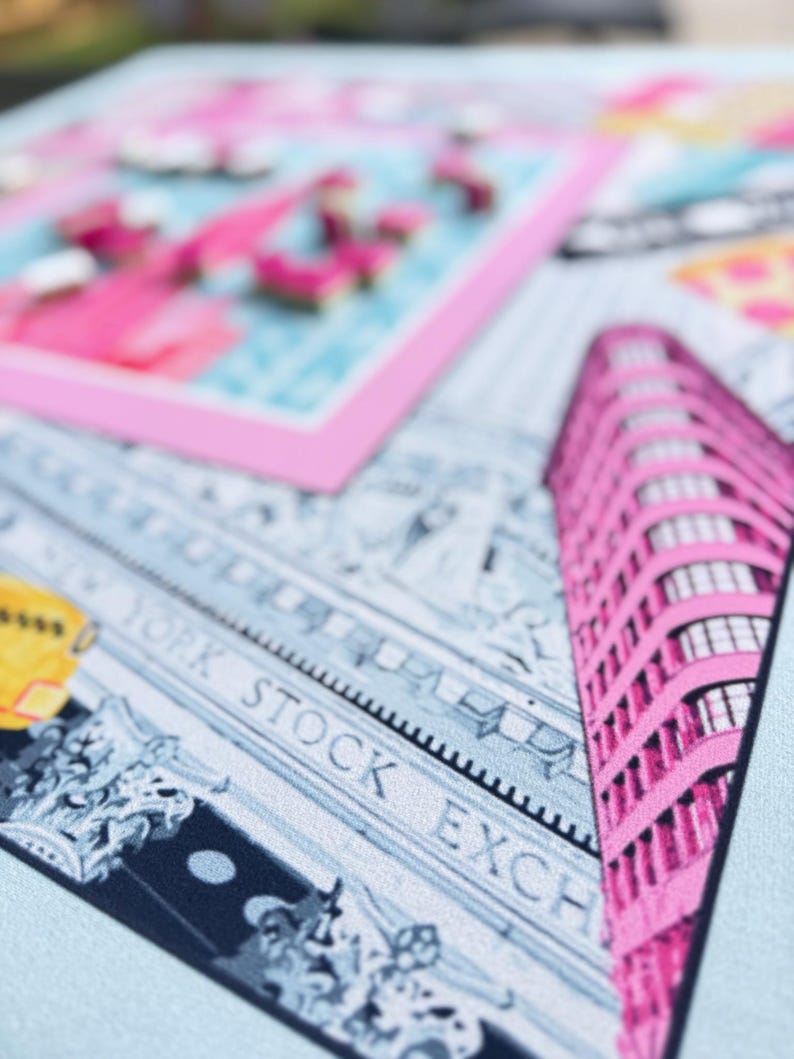 May include: A close-up of a light blue textile with a pink and white design. The design includes a pink building, the words "NEW YORK STOCK EXCHANGE", and a pink framed image with pink flamingos.