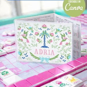 Op de afbeelding: Een gepersonaliseerde Mahjong-kaartinzet met bloemen- en kolibri-illustraties, de naam "ADRIA" wordt in roze weergegeven. Roze en witte Mahjong-tegels omringen de kaart. Tekst bovenaan luidt "Bewerkbare Mahjong Card Insert Printable Reusable".