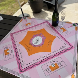 Pu&ograve; includere: Un tabellone di gioco del Mahjong rosa e arancione con la scritta "Press Mahjong" e "Save water drink bubbly". Una bottiglia di champagne verde e un calice da champagne sono sul tabellone. Il tabellone ha un motivo a strisce e le istruzioni del gioco.