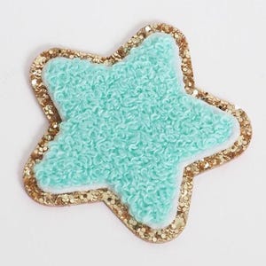 May include: A star-shaped patch with a light blue, textured center, a white border, and a gold glitter outline. This decorative patch is suitable for clothing or accessories.