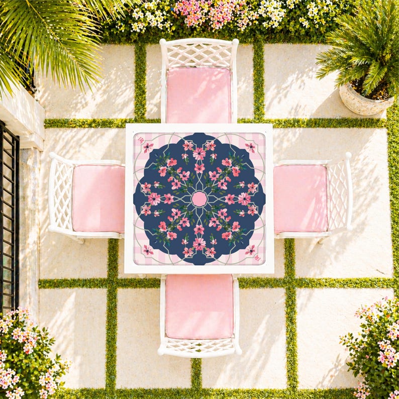 May include: Overhead view of a white outdoor dining set with four chairs and a square table. The table has a navy blue floral design in the center, surrounded by a pink and white striped border. The chairs have white frames and pink cushions.