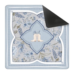 May include: A square doormat with a floral design in shades of blue, gray, and white. The center features a light blue diamond shape with a pair of cream-colored cowboy boots. The mat has a black, non-slip backing.
