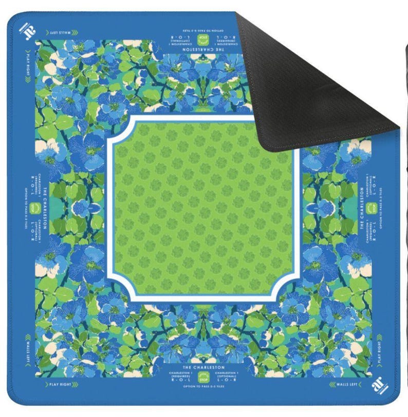 K&ouml;nnte beinhalten: Rechteckige Spielmatte mit blauem und gr&uuml;nem Blumenmuster und einem wei&szlig; umrandeten gr&uuml;nen Mittelteil. Die Matte hat einen blauen Rand mit dem Text "THE CHARLESTON", "WALLS LEFT" und "PLAY RIGHT".