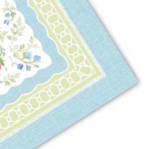 May include: A light blue, floral-patterned placemat with a white and green border. The placemat features a watercolor design of flowers and leaves in shades of pink, blue, and green. The border has a scalloped edge and a textured appearance.