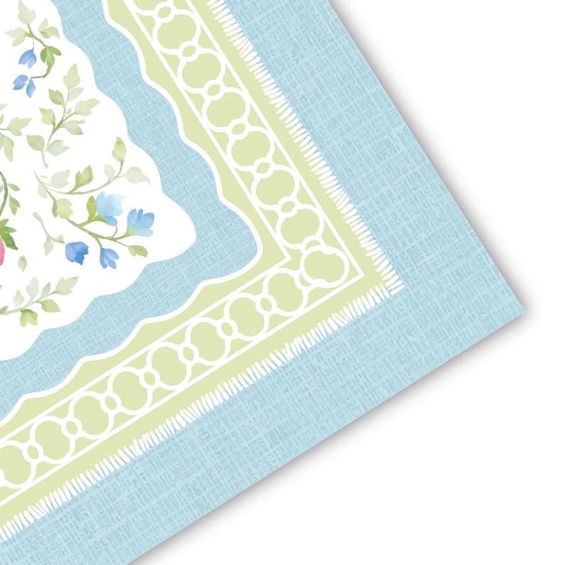 May include: A light blue, floral-patterned placemat with a white and green border. The placemat features a watercolor design of flowers and leaves in shades of pink, blue, and green. The border has a scalloped edge and a textured appearance.