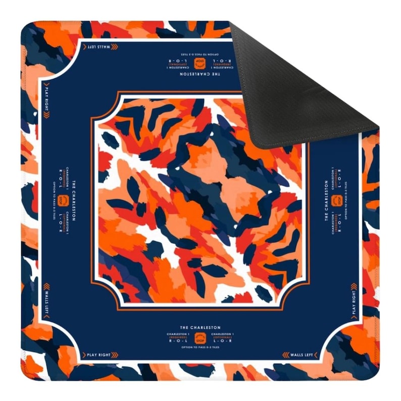 May include: A square game mat featuring a central abstract pattern of orange, dark blue, and white shapes. The border is dark blue with white lines and text including "THE CHARLESTON," "PLAY RIGHT," "WALLS LEFT," and "OPTION TO PASS 0-3 TILES."