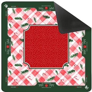 Op de afbeelding: Een vierkante kerstmat met een rood-wit geblokt patroon, zuurstokken en groene dennentakken. Het midden heeft een rood stippenontwerp binnen een wit omrand kader. De randen zijn groen met tekst.