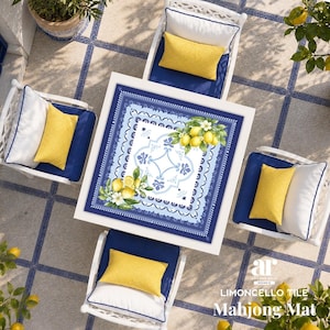 K&ouml;nnte beinhalten: Draufsicht auf einen quadratischen wei&szlig;en Tisch mit einer blau-wei&szlig; gemusterten Matte mit Zitronen und Blumen, umgeben von vier wei&szlig;en St&uuml;hlen mit blauen Kissen und gelben Kissen. Der Text "Limoncello Tile Mahjong Mat" ist sichtbar.
