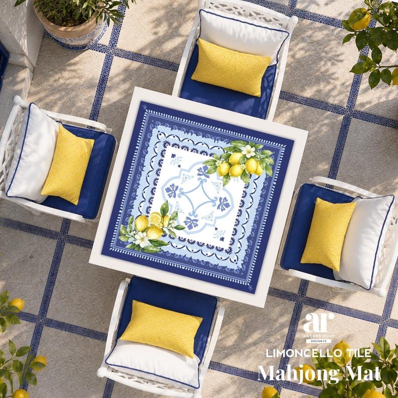 K&ouml;nnte beinhalten: Draufsicht auf einen quadratischen wei&szlig;en Tisch mit einer blau-wei&szlig; gemusterten Matte mit Zitronen und Blumen, umgeben von vier wei&szlig;en St&uuml;hlen mit blauen Kissen und gelben Kissen. Der Text "Limoncello Tile Mahjong Mat" ist sichtbar.