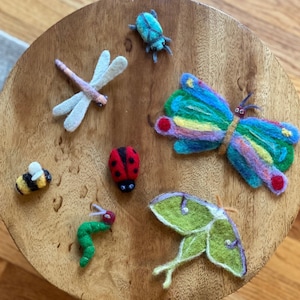 May include: A collection of felt animal and insect crafts, including a butterfly, ladybug, bee, dragonfly, and a moth. The crafts are displayed on a wooden surface.