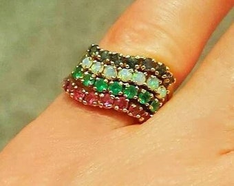 May include: A gold ring with a stack of colourful gemstones. The ring features a row of pink, green, white, and grey gemstones.