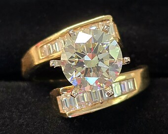 May include: A gold ring with a large, round, clear diamond center stone and smaller, baguette-shaped diamonds on the band.
