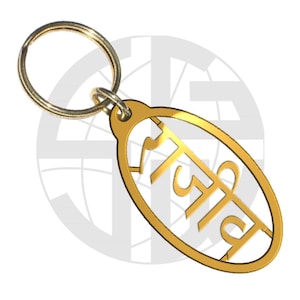May include: A gold-colored metal keychain with a ring and an oval-shaped tag. The tag has the word "अजिब" written in Hindi script.