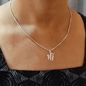 Puede incluir: Un collar de cadena de plata con un colgante de plata que presenta el símbolo "Ik Onkar" en un diseño simple y elegante.