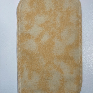 May include: A beige fabric square with a white stitched border. The fabric has a mottled, tie-dye pattern.