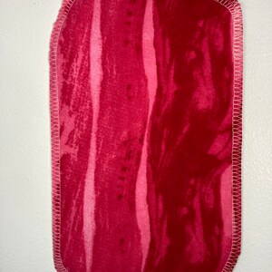 May include: A red fabric rectangle with a white stitched border. The fabric has a marbled pattern with shades of pink and red.