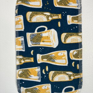 May include: A blue fabric with a white and yellow pattern of beer bottles and mugs. The fabric has a white stitched border.