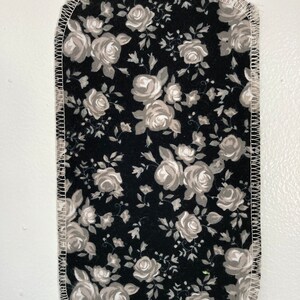 May include: A black fabric square with a white floral pattern. The fabric has a white stitched border.