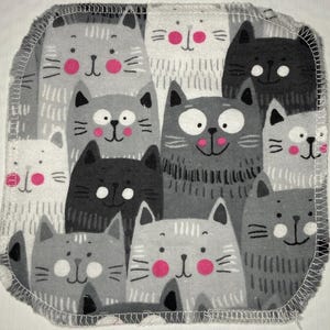Puede incluir: Tela cuadrada gris y blanca con un patrón repetido de gatos de dibujos animados. Los gatos tienen varios tonos de gris, con narices rosas y caras sonrientes. Los bordes de la tela están acabados con un borde blanco cosido.