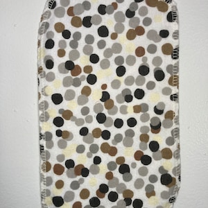 May include: A white fabric square with a brown, black, and gray polka dot pattern. The fabric is sewn around the edges.