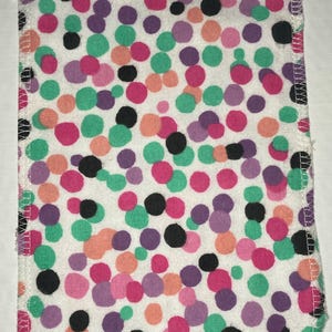 May include: A white fabric square with a polka dot pattern. The dots are in various colors, including pink, green, purple, and black.