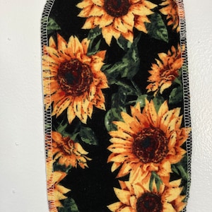 May include: A black fabric square with a white stitched border features a repeating pattern of yellow sunflowers with brown centers on a dark green background.
