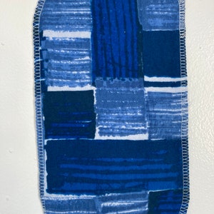 May include: A blue and white fabric scrap with a geometric pattern. The fabric is sewn around the edges with white thread.