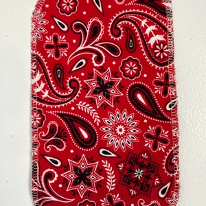 May include: Red bandana fabric with a white paisley pattern. The fabric is sewn around the edges with white thread.