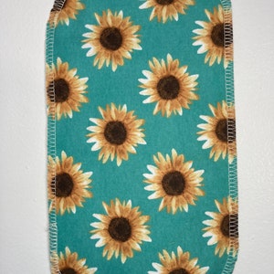 May include: A teal fabric with a white stitched border features a repeating pattern of brown and yellow sunflowers.