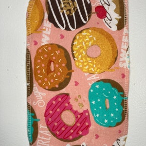 Puede incluir: Tela rosa con un patrón de donuts. Los donuts son de varios colores y tienen diferentes coberturas, incluyendo chispas, chocolate y glaseado. El texto "Sweet Treats" y "Sugar" está impreso en la tela.