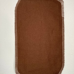 May include: A brown fabric rectangle with white stitching around the edges.