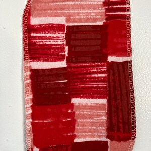 Puede incluir: Tela roja y blanca con un patrón geométrico. La tela tiene un borde cosido blanco.