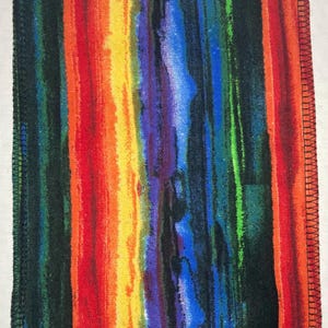 May include: A colorful fabric with a rainbow stripe pattern. The fabric has a black border with a zig-zag stitch.