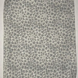 May include: A white fabric square with a gray floral pattern. The fabric has a stitched edge.